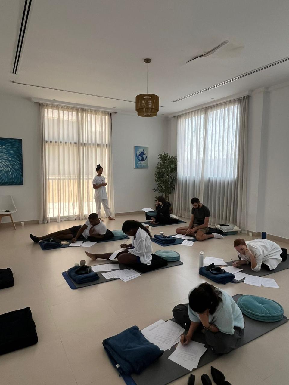 Participants writing on worksheets on mats in a bright, sunlit workshop room